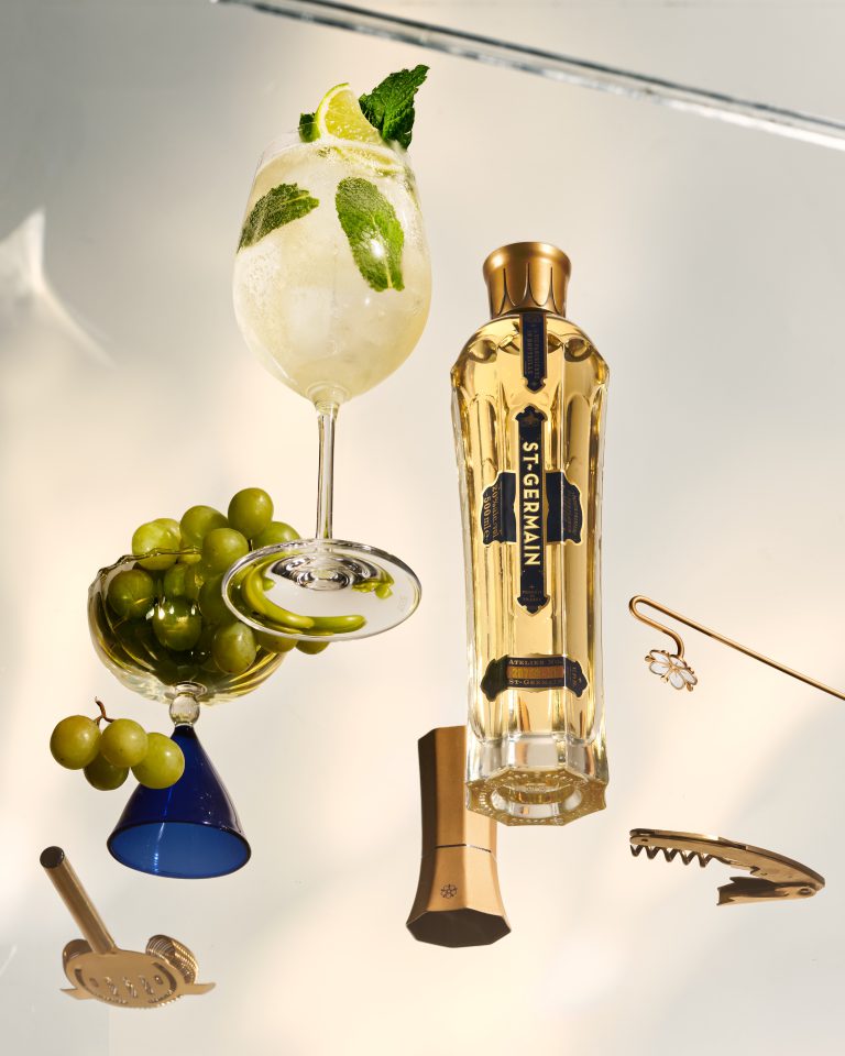 St-Germain elderflower liqueur bottle with martini glass and olives Hugo Spritz Cocktail on minimal studio set shot from below
