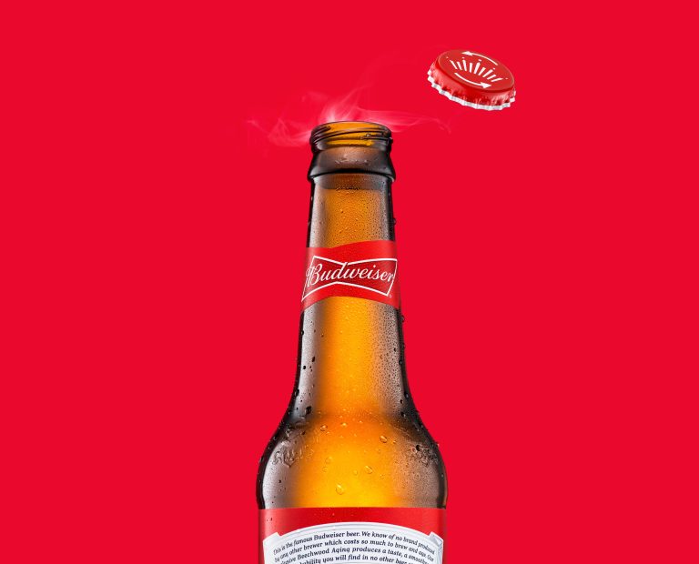 Budweiser beer bottle with cap popping against red background, advertising campaign image