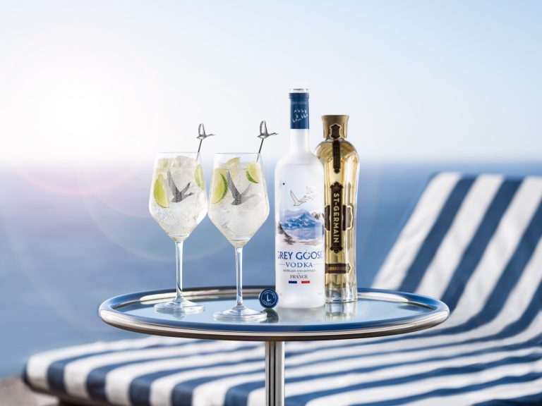 Grey Goose vodka bottle and cocktails on table in front of towelled sun lounger with ocean backdrop in Cape Town