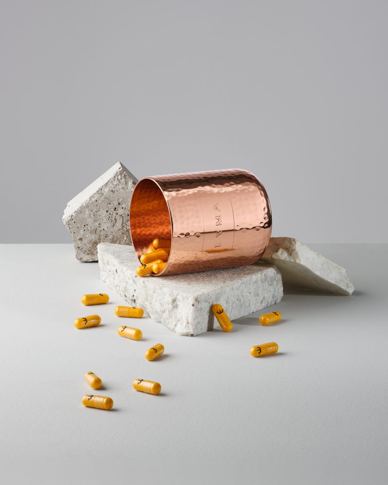 Lyma supplement capsules spilling from copper container on minimal studio set