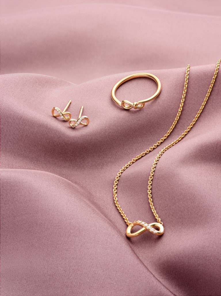 Pandora gold necklace and earrings on soft pink fabric, jewellery still life