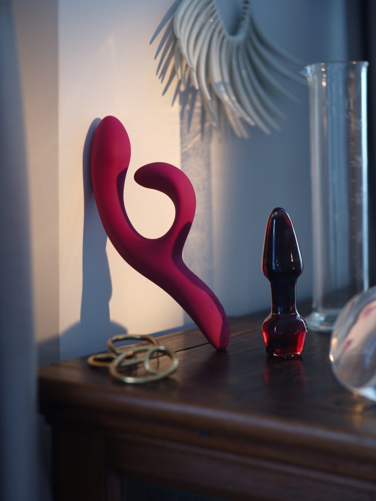 Red sculptural intimate object with glass vessel and metallic accessories on domestic surface
