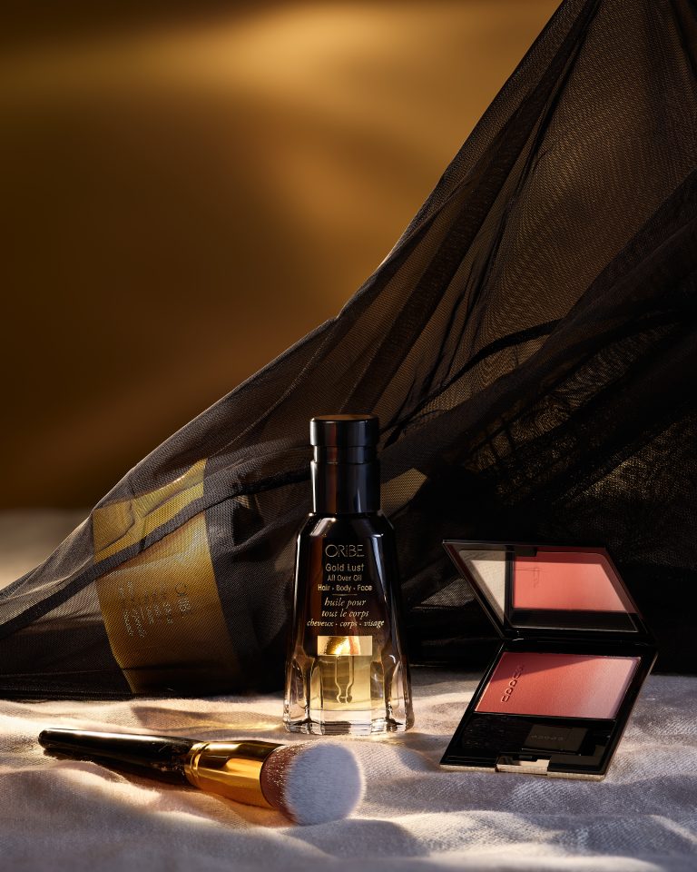 Perfume bottle and makeup palette under black sheer fabric in studio still life