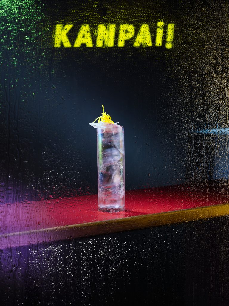 Tall cocktail glass on bar with rain-like droplets and dark background, magazine cover image