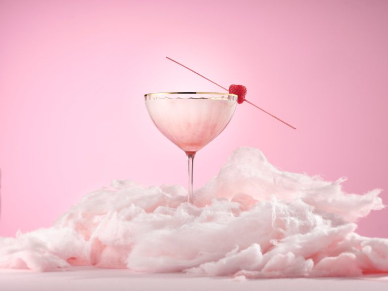 Pink cocktail glass on cloud-like surface with pink background, stylised drinks photography