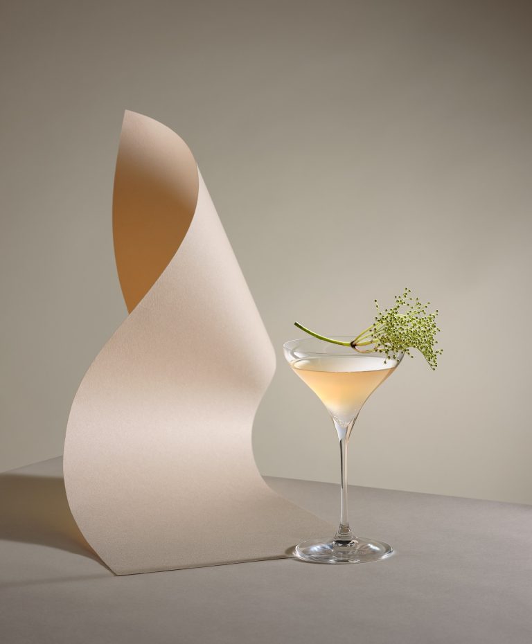 Martini glass beside curved sculptural form on minimal set, conceptual editorial still life