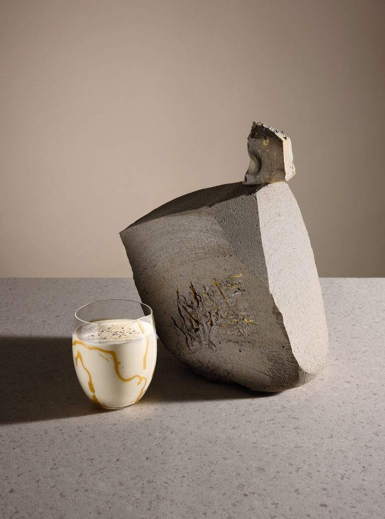 Textured sculptural block with cocktail glass on neutral background, artistic drinks composition