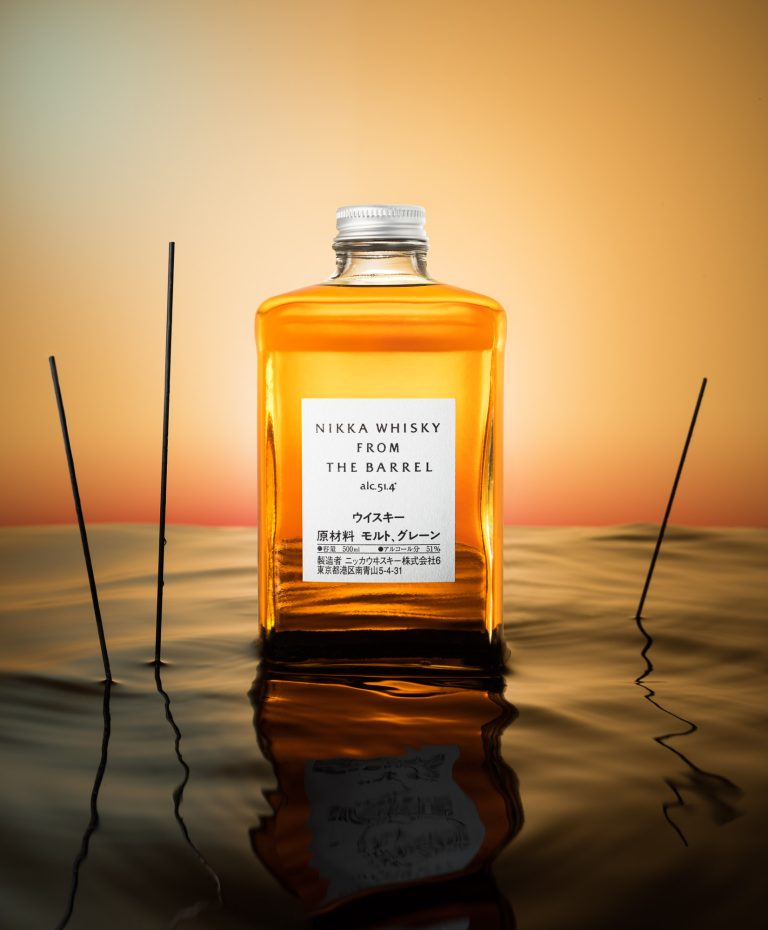 Nikka whisky bottle on reflective water surface with warm sunset lighting