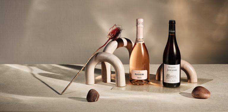 Rosé wine bottle with sculptural props on neutral background, editorial still life