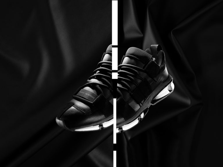 Black Adidas trainer suspended against dark sculptural backdrop, studio still life