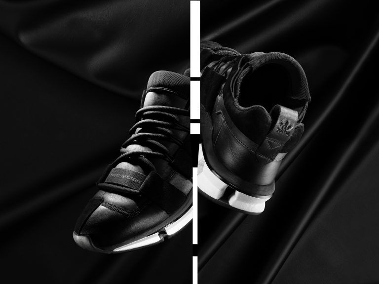 Adidas black trainer pair against dark fabric backdrop with strong lighting