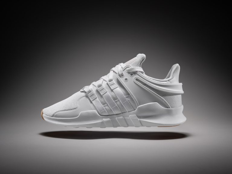 White Adidas trainer suspended against dark gradient background, studio footwear photography