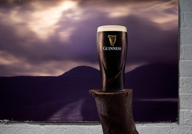 Guinness full pint glass in front of printed Irish mountain landscape, conceptual studio setup