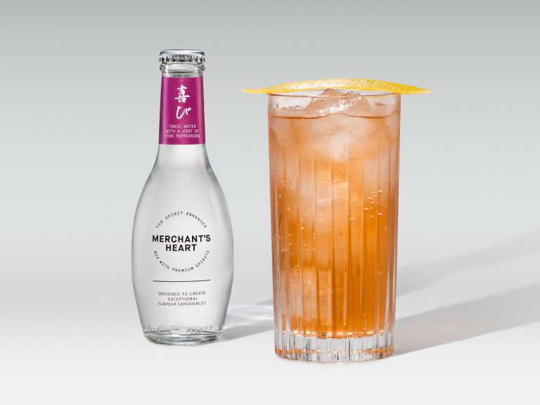 Merchant’s Heart pink mixer bottle with tall amber iced drink and citrus garnish