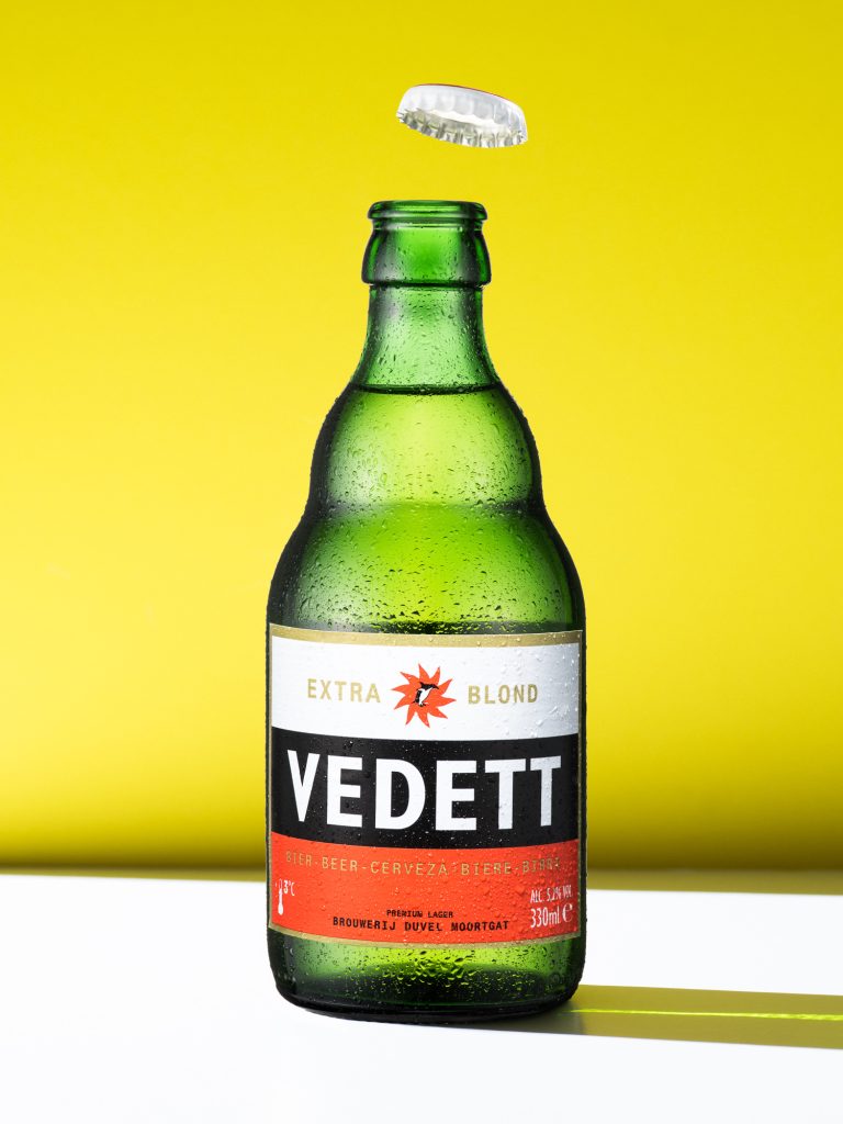 Vedett beer bottle on yellow background with strong shadow, product still life
